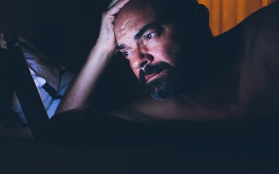 A person with beard and mustache in bed looking concerned